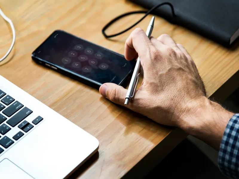 Twee handen met een smartphone boven een toetsenbord